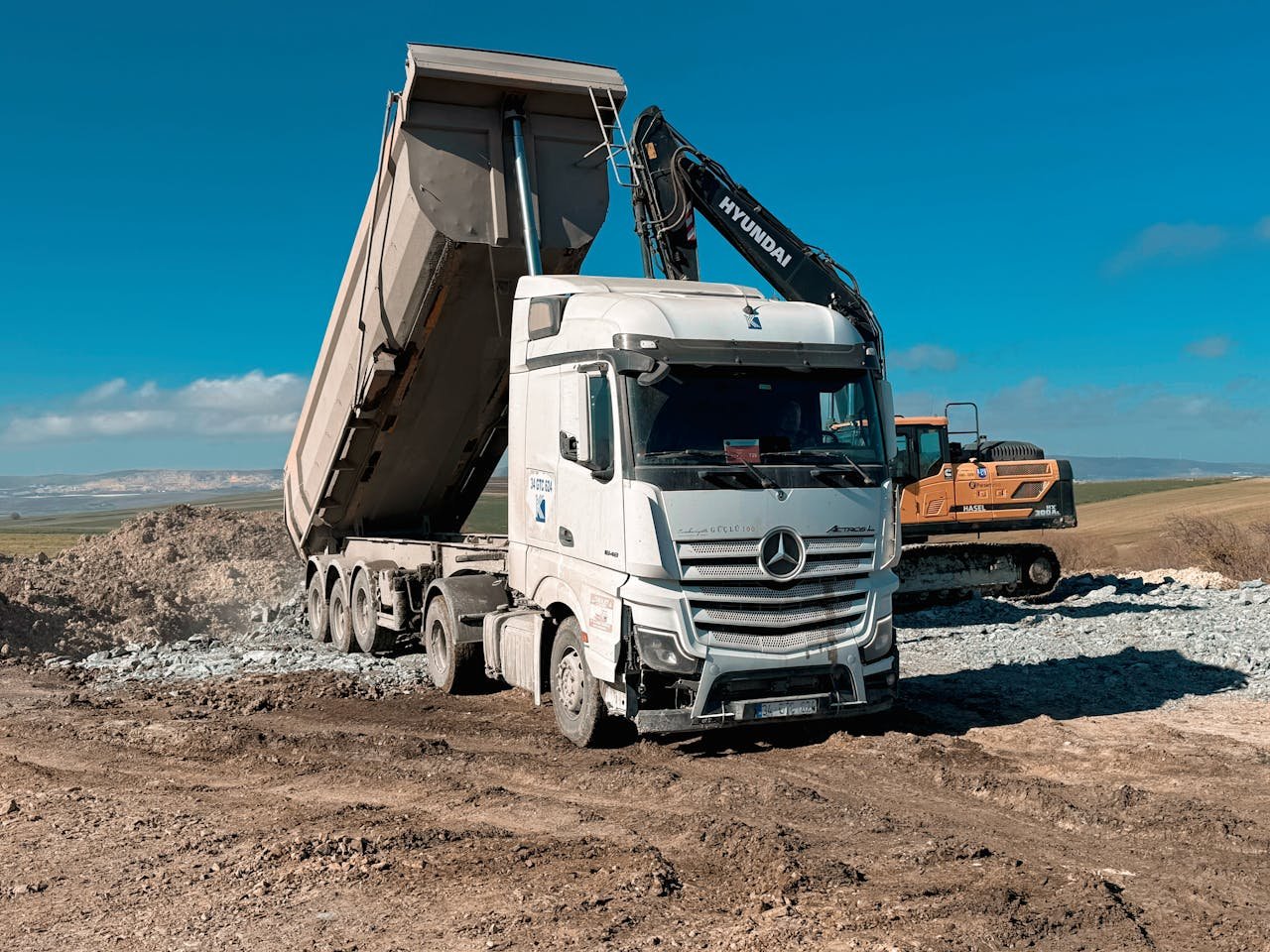 Heavy-duty dump truck and excavator operating on a sunny day at a construction site.